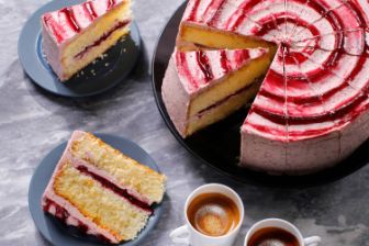Whole layered cake with red and white swirl icing, shown with several sliced portions on plates and two cups of espresso.