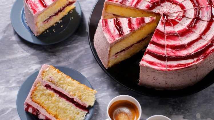 Whole layered cake with red and white swirl icing, shown with several sliced portions on plates and two cups of espresso.