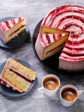 Whole layered cake with red and white swirl icing, shown with several sliced portions on plates and two cups of espresso.