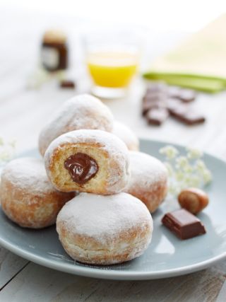 Chocolate beignets dusted with powdered sugar, one cut open showing white chocolate cream filling