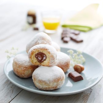 Chocolate beignets dusted with powdered sugar, one cut open showing white chocolate cream filling