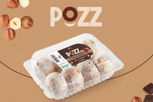 Tray of powdered mini beignets placed in front of the POZZ brand logo on a light brown background with hazelnuts.