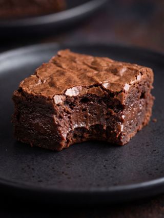Close‑up of a fudgy chocolate brownie with a bite taken out, showing a rich, gooey center on a dark plate