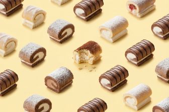 Assorted mini roll cakes in various flavors arranged in a repeating pattern on a yellow background, with one roll cut open to show the filling.