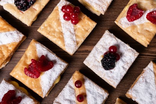 Square pastry pieces dusted with powdered sugar and topped with assorted berries arranged on a wooden surface.