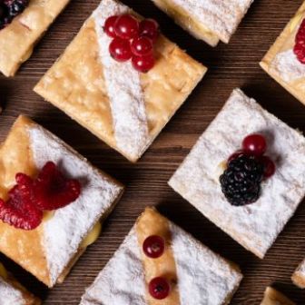 Square pastry pieces dusted with powdered sugar and topped with assorted berries arranged on a wooden surface.