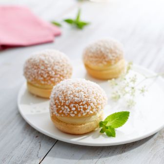Three round pastries filled with cream and topped with coarse sugar, arranged on a white plate with mint leaves.