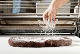 Hand sprinkling flour over chocolate dough in a bakery setting
