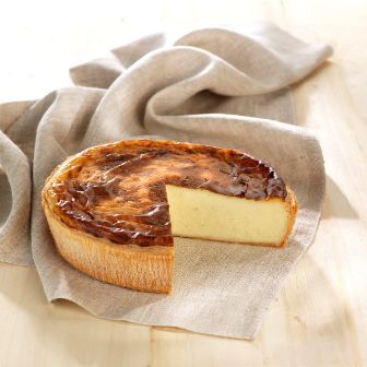 Round baked custard tart with a glossy top and one slice removed, displayed on a beige cloth.