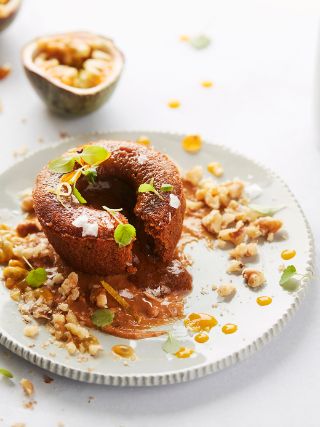 Caramel lava cake on a white plate with oozing caramel, nuts, herbs, and passion fruit garnish