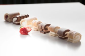 Assorted mini roll slices in various flavors arranged in a line with a fresh strawberry on a white surface