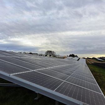 Large outdoor array of angled solar panels extending across a grassy area under a cloudy sky.