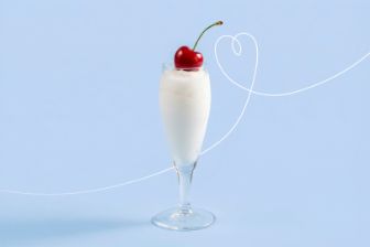 Tall glass filled with a white sorbissimo ice cream dessert topped with a red cherry, placed against a light blue background.