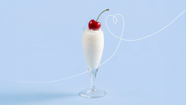 Tall glass filled with a white sorbissimo ice cream dessert topped with a red cherry, placed against a light blue background.