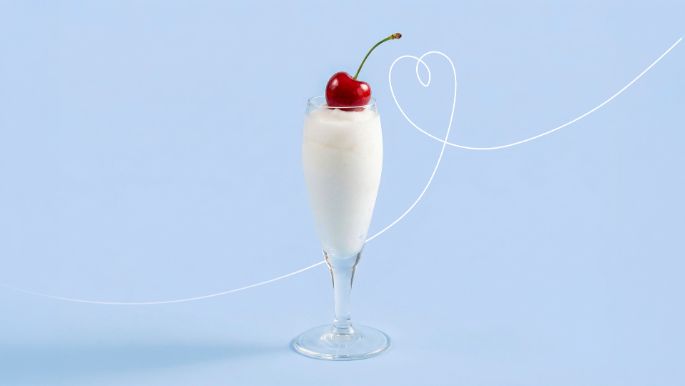 Tall glass filled with a white sorbissimo ice cream dessert topped with a red cherry, placed against a light blue background.