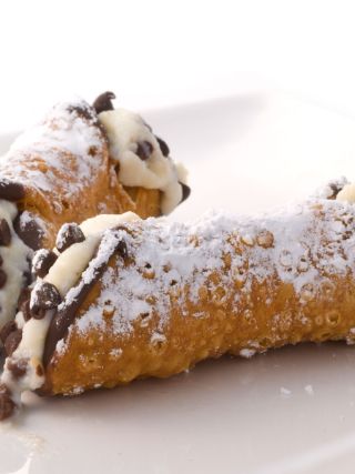 Two chocolate chip cannoli filled with sweet ricotta cream and dusted with powdered sugar
