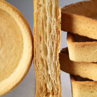 Close‑up of various empty pastry shells and layered dough sections, including round and square shapes.