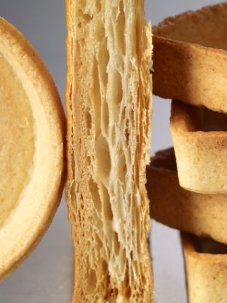 Close‑up of various empty pastry shells and layered dough sections, including round and square shapes.