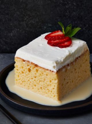 Slice of tres leches cake topped with whipped cream, strawberries, and mint on a dark plate
