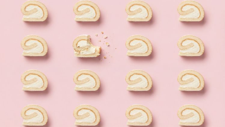 Pattern of vanilla filled roll slices on a pink background with one bitten piece and crumbs.